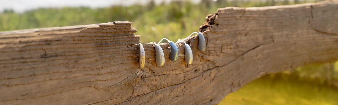Verschiedene Hoergeraete auf einem Holzbalken haengend